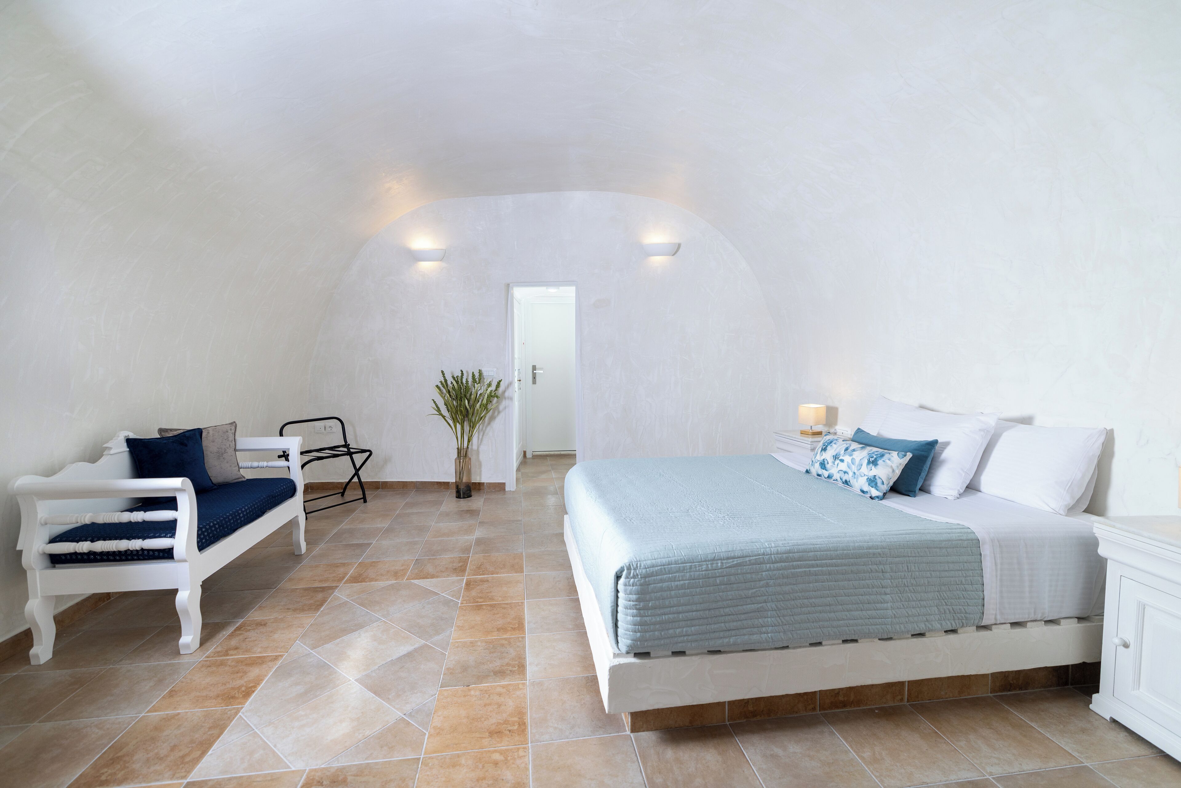 Un dormitorio con una cama, un banco, una silla y una planta en maceta.