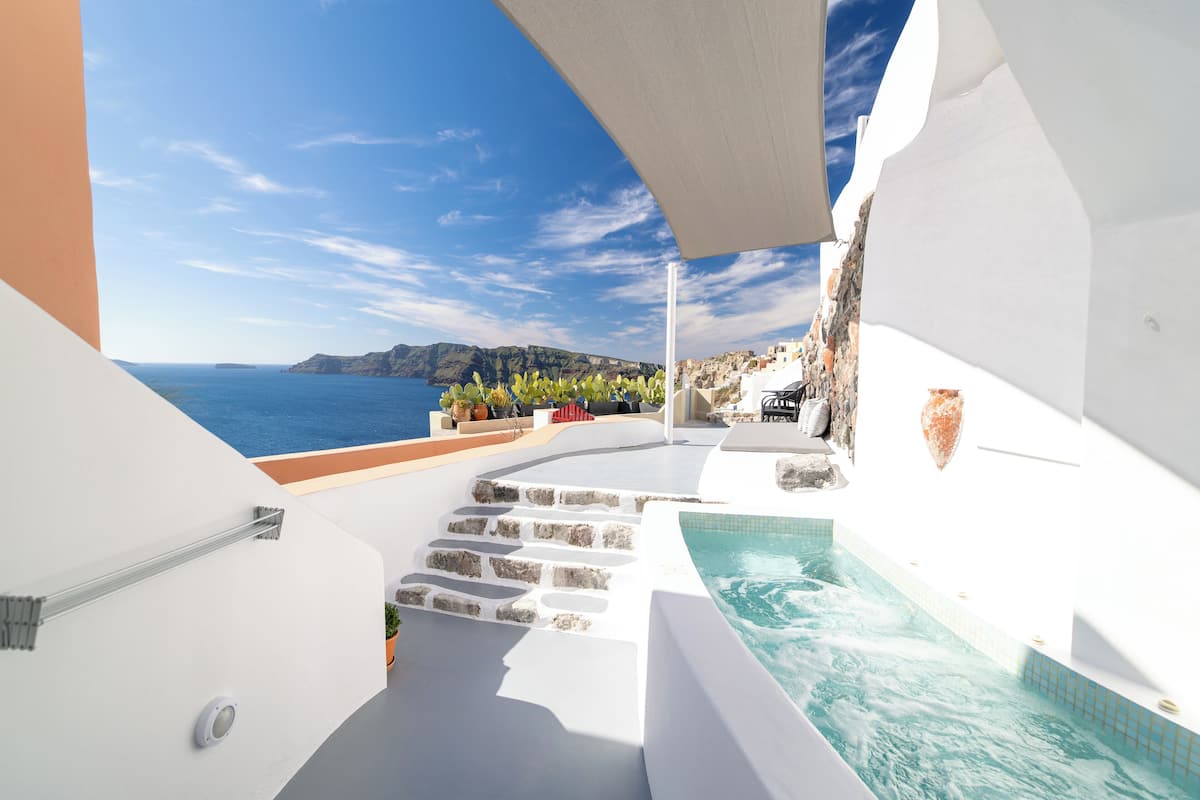 Un espace piscine extérieur moderne, avec vue sur la mer et un bâtiment blanc dont des marches descendent jusqu’à l’eau.