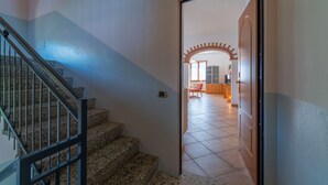 A staircase leading to a room with a tiled floor and a door leading to a living area with a red chair and a table. - Antico Lavatoio Valbrona (Valbrona)