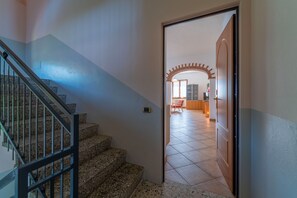 A staircase leading to a room with a tiled floor and a door leading to a living area with a red chair and a table. - Antico Lavatoio Valbrona (Valbrona)