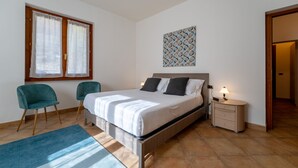 A bedroom with a bed, two chairs, a bedside table with a lamp, and a window with curtains. - Antico Lavatoio Valbrona (Valbrona)