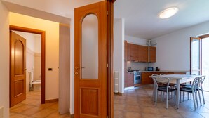 A modern kitchen with wooden cabinets, a dining table with chairs, and a visible bathroom in the background. - Antico Lavatoio Valbrona (Valbrona)