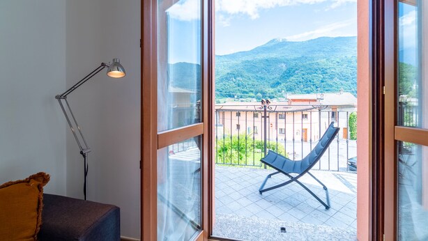 A room with a large sliding glass door leading to an outdoor balcony with a chair and a mountain view. - Antico Lavatoio Valbrona (Valbrona)