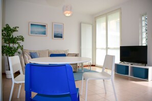 Una sala de estar moderna con una mesa redonda, sillas azules, un sofá, un televisor y dos cuadros en la pared.