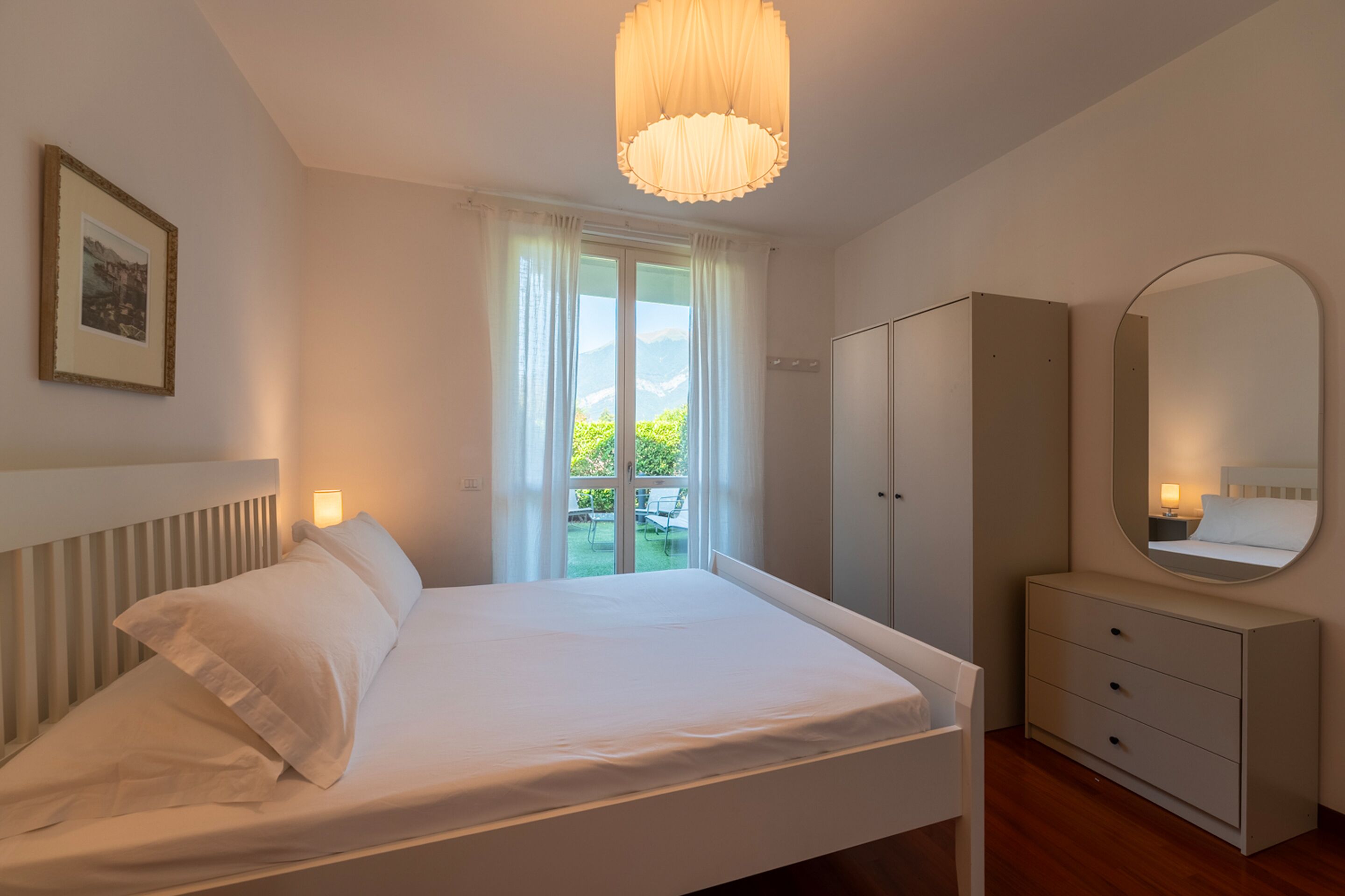 Un dormitorio con cama, armario, espejo y ventana con cortinas.
