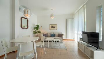 Una sala de estar moderna con comedor, un sofá, un televisor y un ventanal grande.