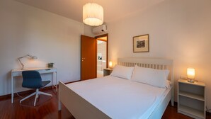 Ett hotellrum med en säng, ett skrivbord, en stol, ett sängbord med en lampa och en tavla på väggen.