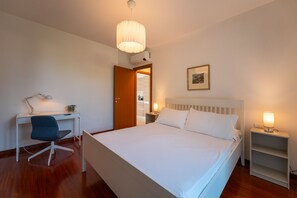 Ein Hotelzimmer mit einem Bett, einem Schreibtisch, einem Sessel, einem Nachttisch mit Lampe und einem Bild an der Wand.