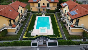En bostadsbyggnad med en central pool, omgiven av välskötta trädgårdar och balkonger med solpaneler.