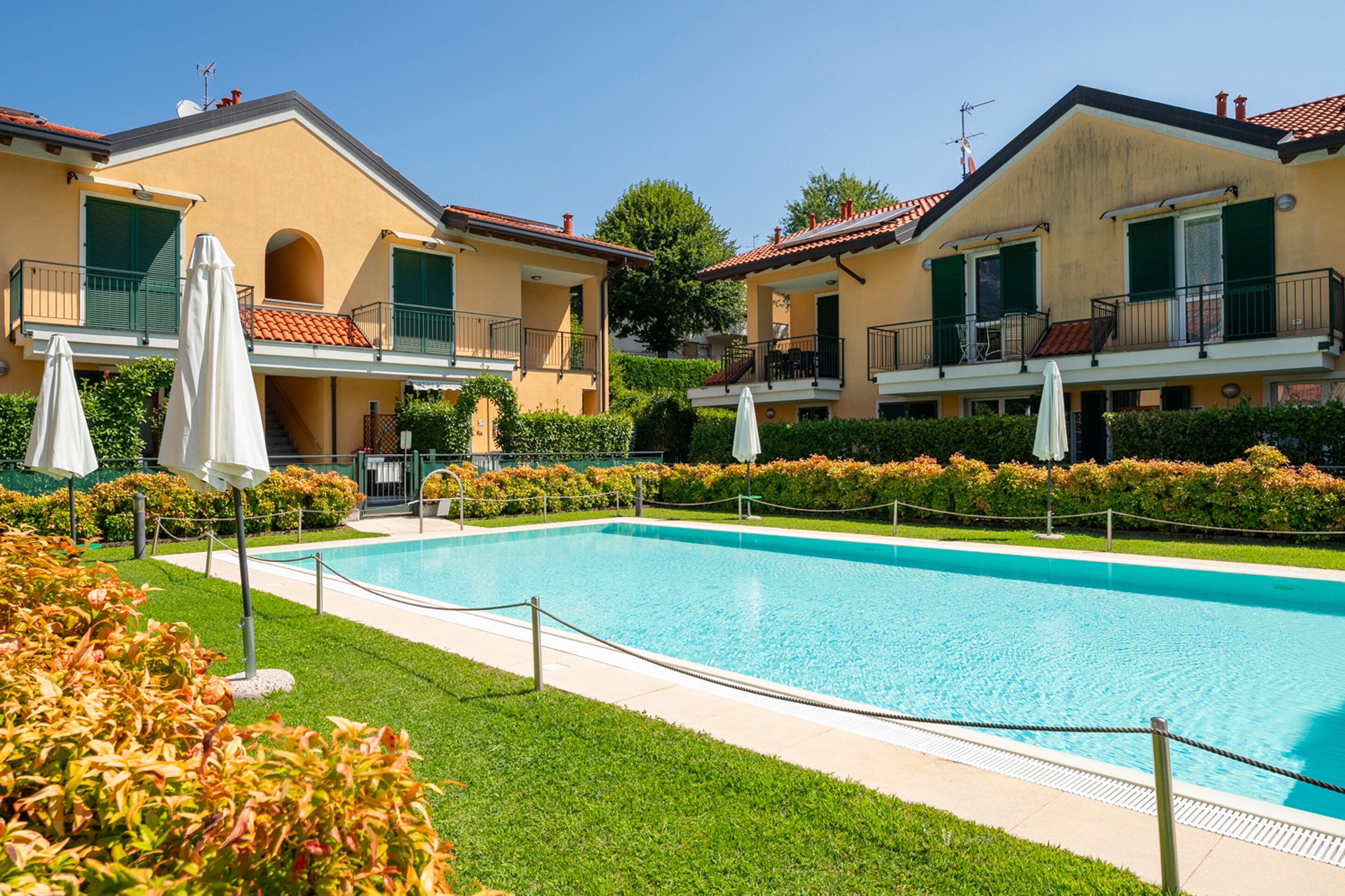 Una piscina rodeada por un césped cuidado y una hilera de edificios de dos pisos con balcones.