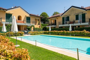 Une piscine entourée d’une pelouse bien entretenue et d’une rangée d’immeubles à deux étages dotés de balcons.