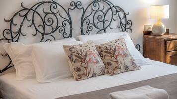Una cama bien hecha con sábanas blancas, dos almohadas decorativas con estampado floral y un cabecero de metal con diseños intrincados.