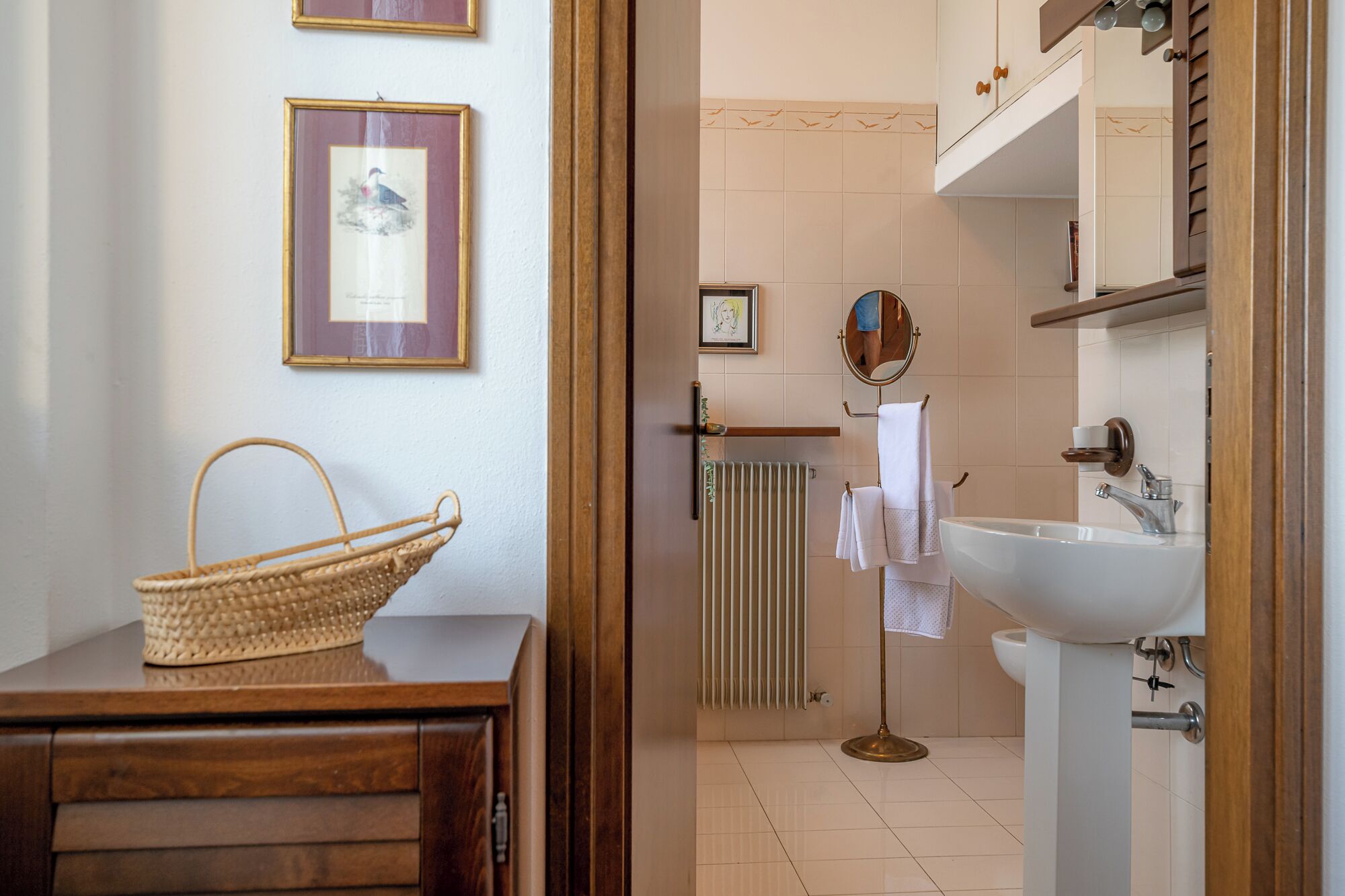 Une salle de bain avec un lavabo blanc, un miroir et un porte-serviettes. On y trouve un panier en osier posé sur un comptoir en bois.