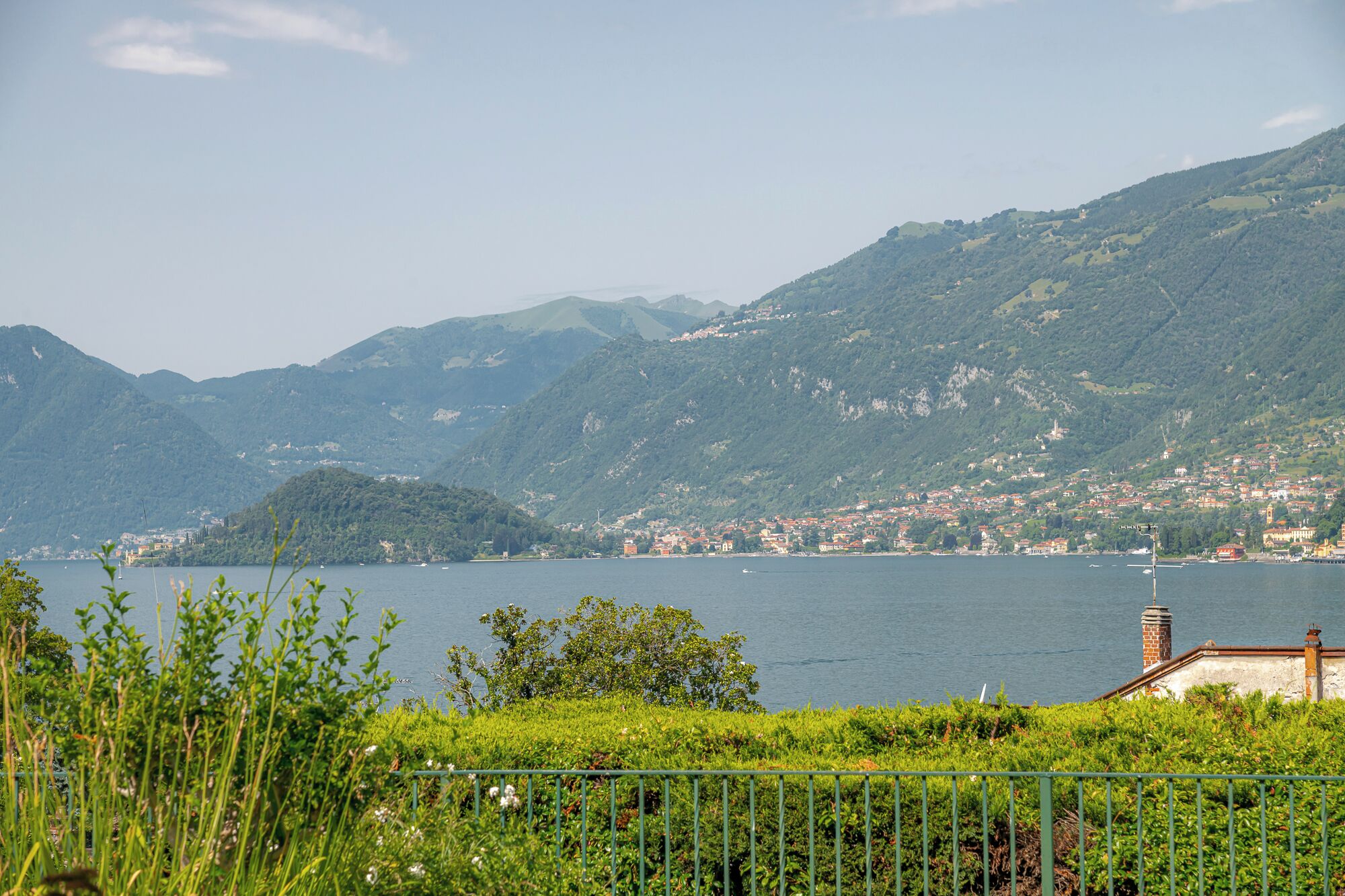 A lakeside view with mountains, a small town, and a building with a chimney.