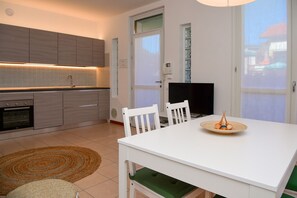 Une cuisine moderne dotée d’appareils électroménagers intégrés, un coin repas avec une table et des chaises blanches, et un téléviseur.