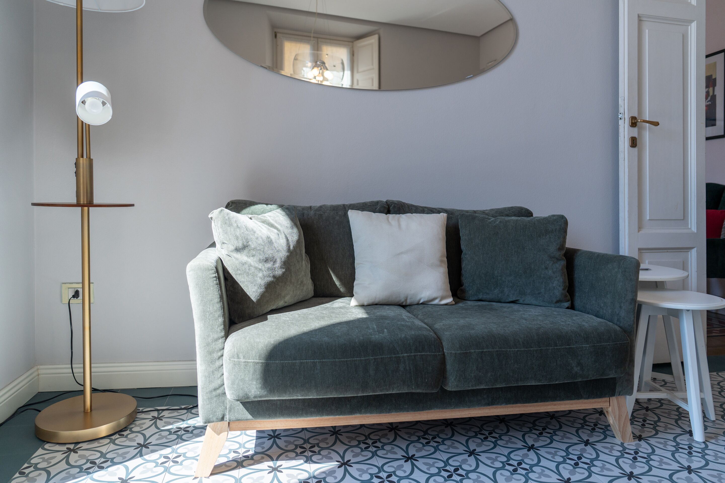 A grey sofa with cushions, a floor lamp, a small table, and a patterned floor.