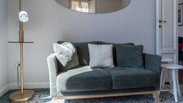 A grey sofa with cushions, a floor lamp, a small table, and a patterned floor.