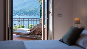 A bedroom with a bed, a nightstand, a lamp, and a view of a balcony with a railing and a chair.