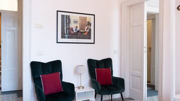Een kamer met twee donkergroene fauteuils met rode kussens, een klein witte bijzettafeltje met een lamp en een ingelijste foto aan de muur.