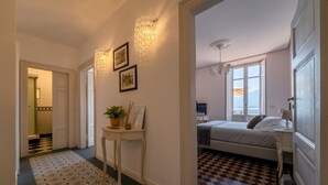 En hall med ett mönstrat golv, ett litet bord med en växt och en säng med ett rutigt golv i det intilliggande rummet.