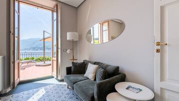 Una habitación con un sofá gris, una mesita blanca pequeña, un espejo redondo y vistas a un balcón con barandilla.