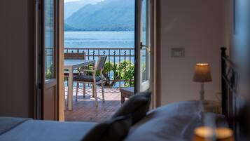 Habitación de hotel con una cama, una mesita de noche con lámpara y vistas a un balcón con mesa y sillas.