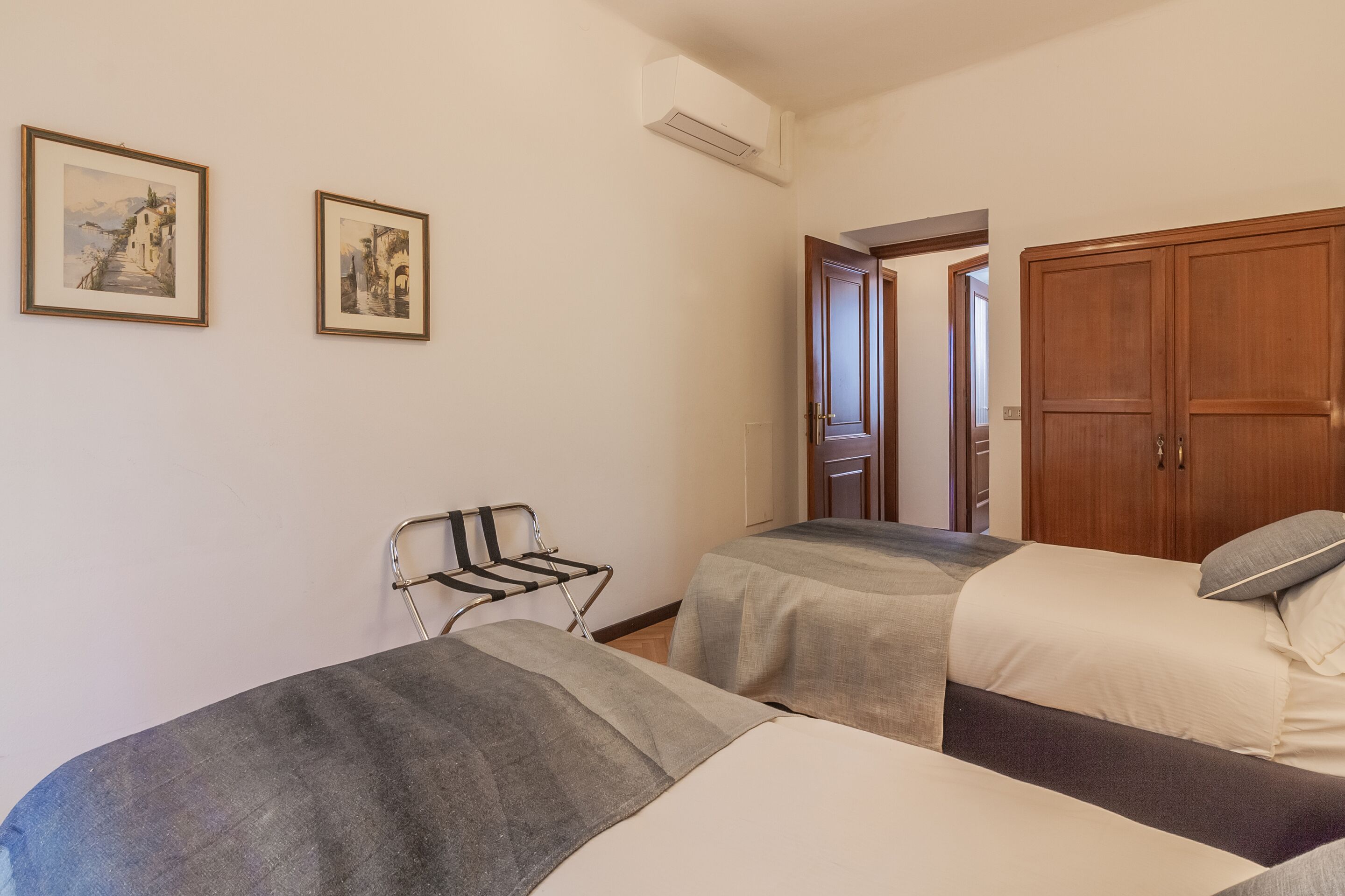 A hotel room with two beds, a chair, and two framed pictures on the wall.