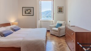 Ein Schlafzimmer mit Bett, Sessel, Kommode und Fenster mit Bergblick.