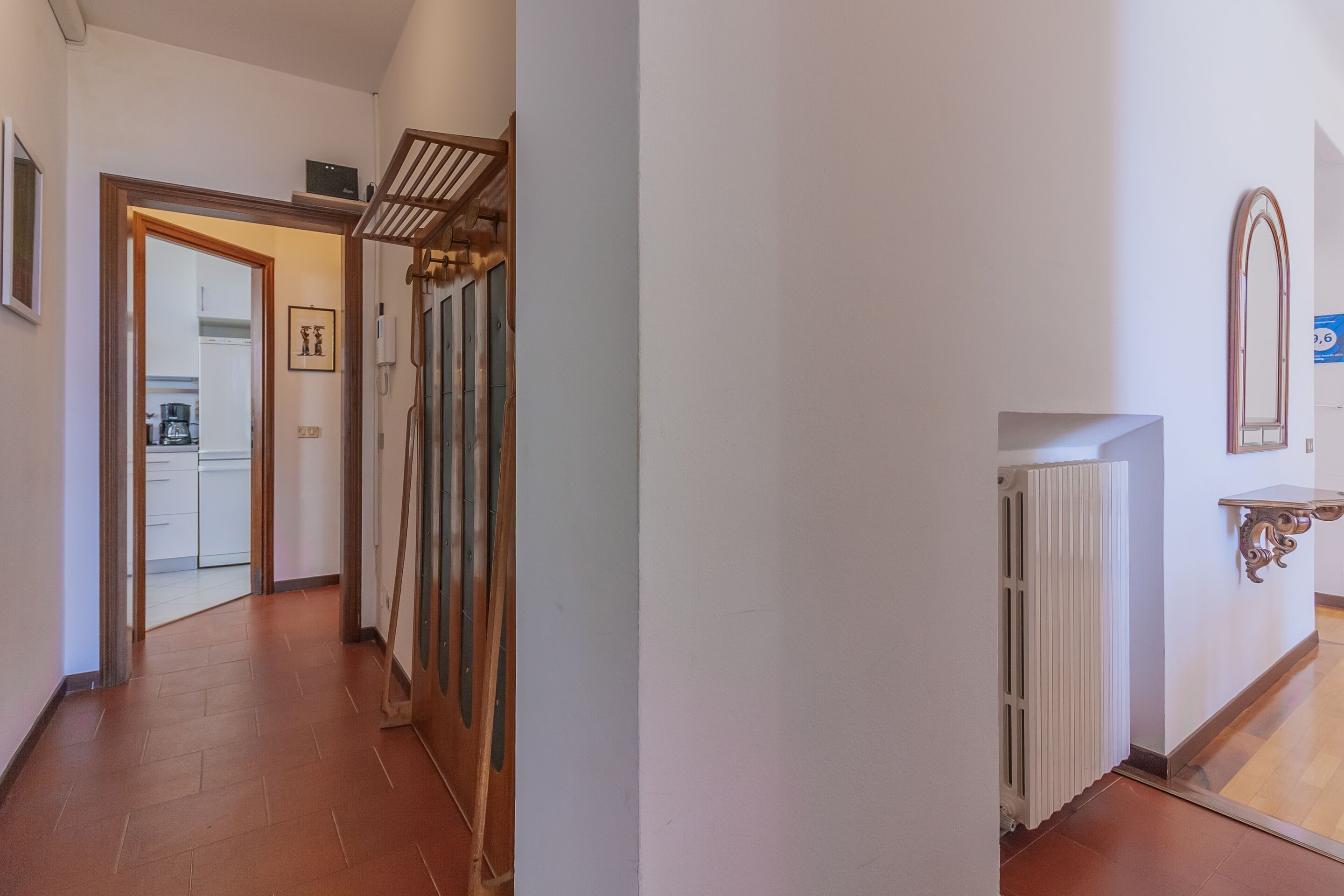 A hallway with a radiator, a mirror, and a door leading to a kitchen.