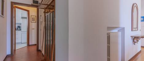 A hallway with a radiator, a mirror, and a door leading to a kitchen.