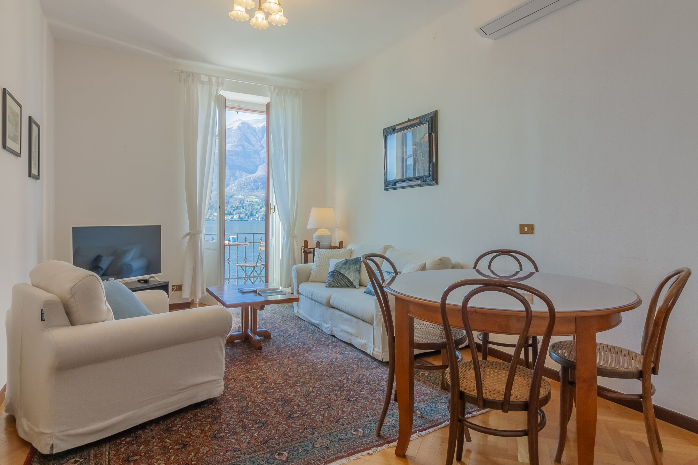 A living room with a sofa, TV, dining table, chairs, and a view of mountains through a window.
