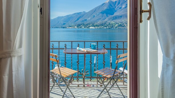 Ein Balkon mit Tisch und Stühlen mit Blick auf einen See und Berge.