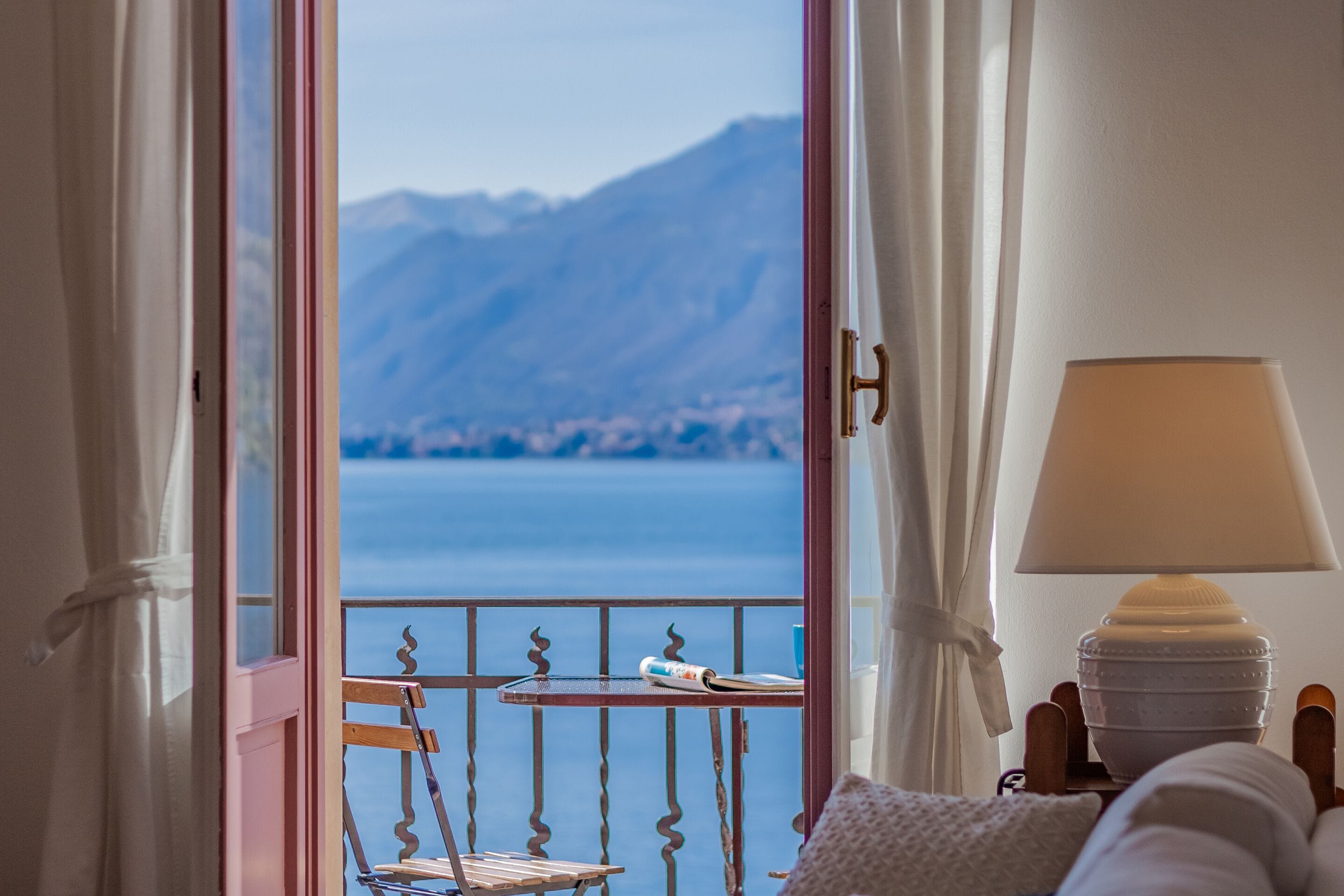 Habitación con vista a un cuerpo de agua y montañas. Hay una mesa con una lámpara y una silla.