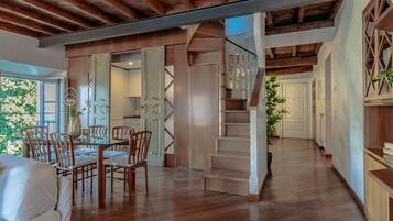 Uma sala de estar ampla com escada de madeira, mesa de jantar com cadeiras e vista para o exterior.