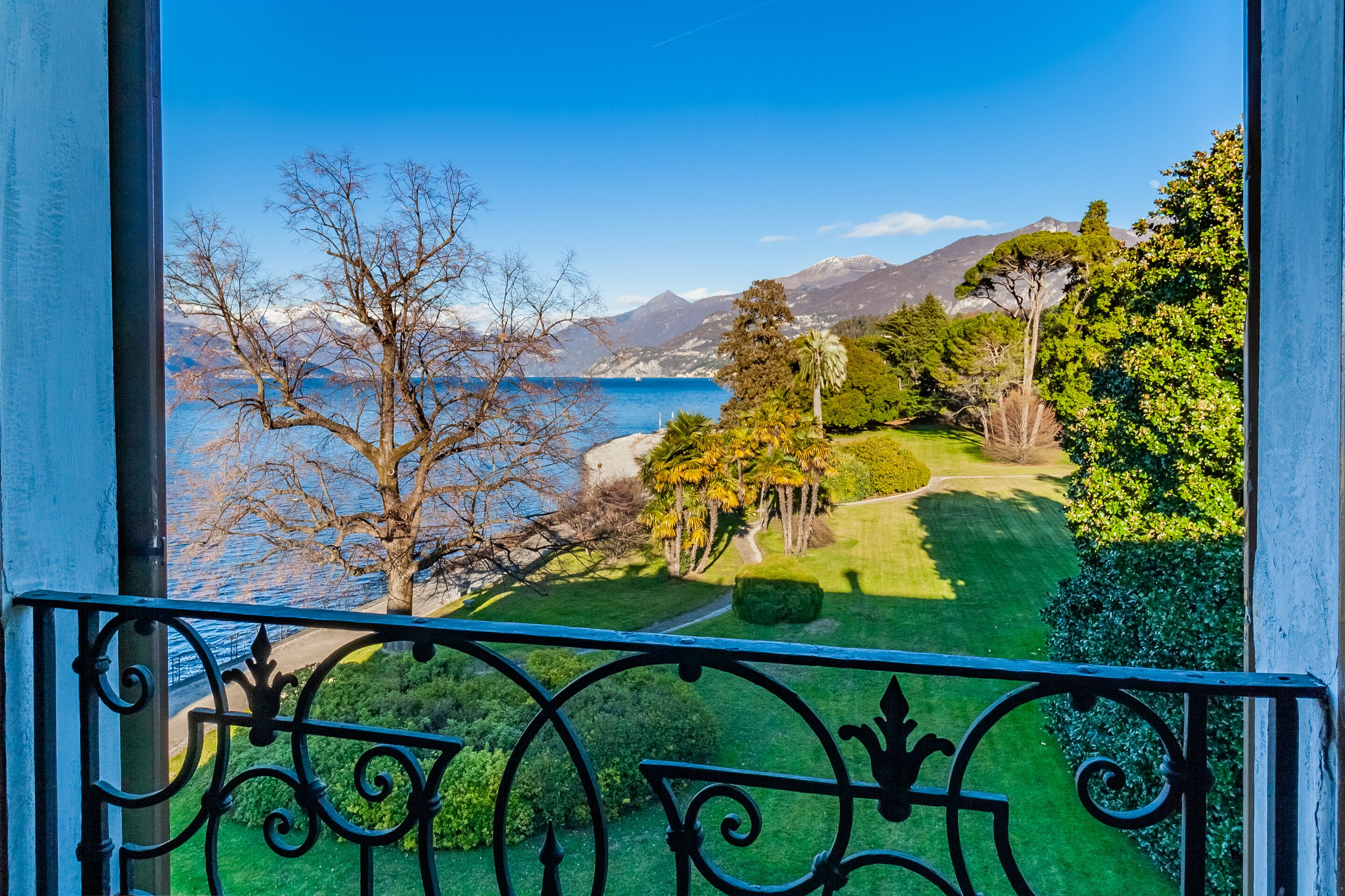 Uma varanda com vista para uma paisagem costeira, incluindo um corpo de água, montanhas e um gramado bem cuidado.