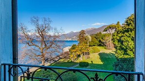A balcony with a view of a coastal landscape, including a body of water, mountains, and a well-maintained lawn. - Domus Elena Lakeview (Bellagio)