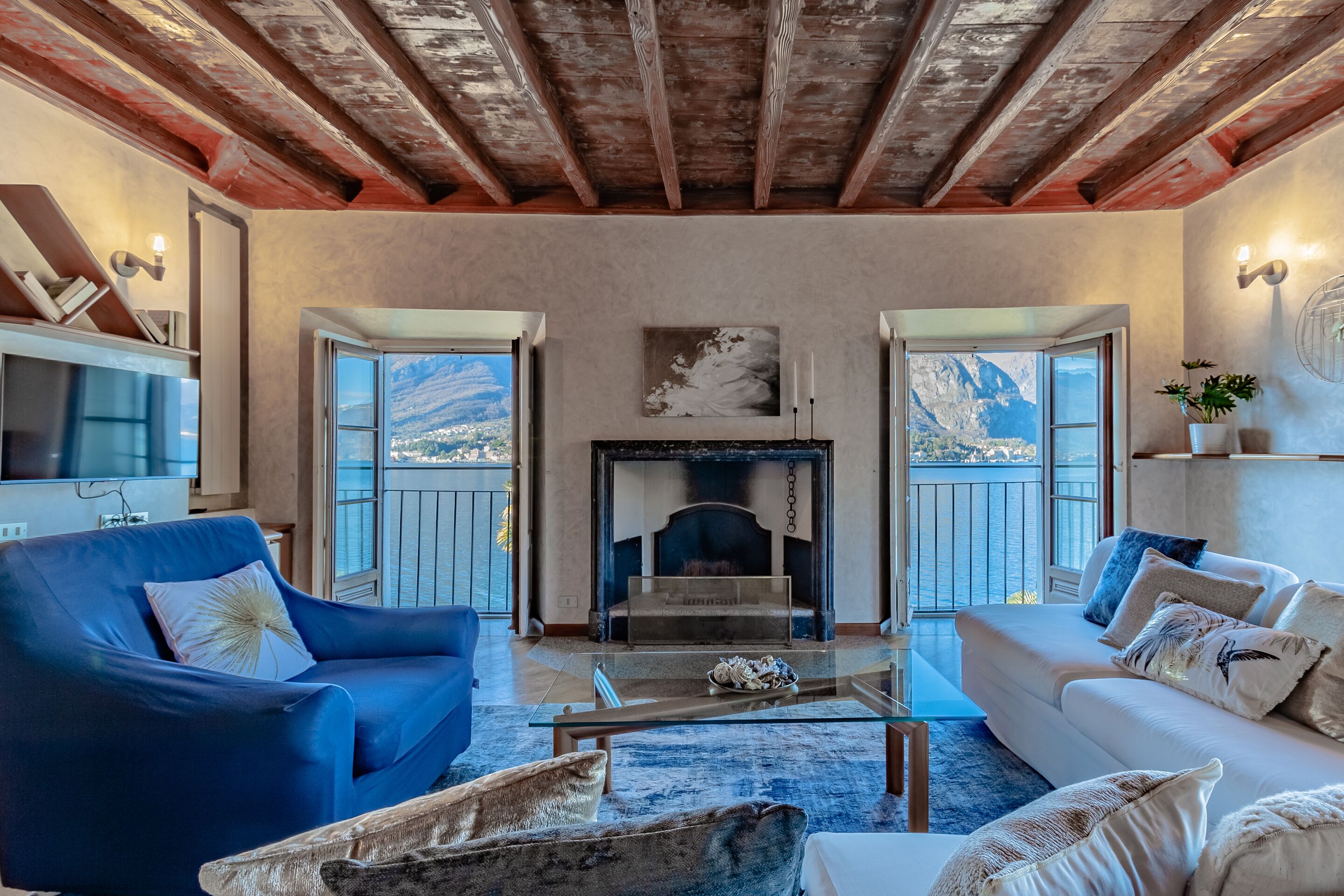 Ein Wohnzimmer mit Kamin, blauen und weißen Sofas und Blick auf die Berge durch offene Fenster.