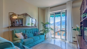 Un salon spacieux avec un canapé de couleur turquoise, un tapis rond et une grande fenêtre donnant sur une vue imprenable sur une montagne.