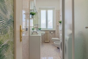 Un baño moderno con un lavamanos, inodoro y una ventana sobre el inodoro. Hay plantas en el alféizar de la ventana y un perchero sobre el lavamanos.