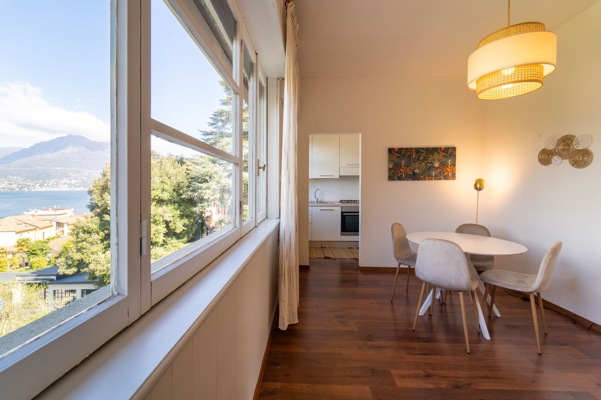 Una habitación con un ventanal grande, una mesa de comedor con sillas, una zona de cocina y una lámpara colgante.