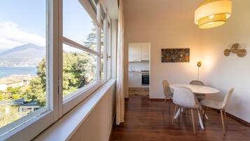 Una habitación con un ventanal grande, una mesa de comedor con sillas, una zona de cocina y una lámpara colgante.