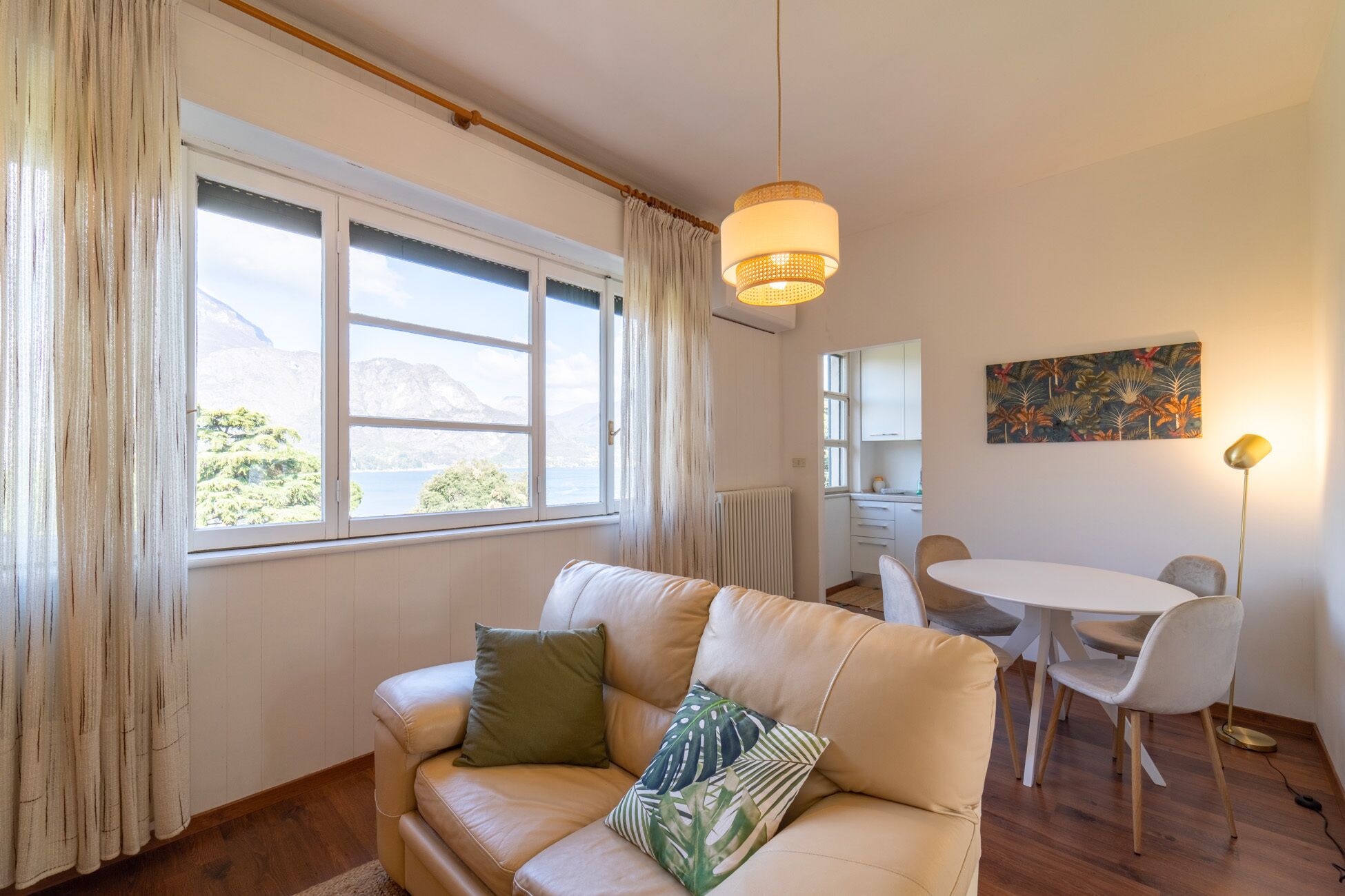 Una sala de estar acogedora con un sofá color beige, una mesa de comedor con sillas, una lámpara colgante y vistas a montañas a través del ventanal.