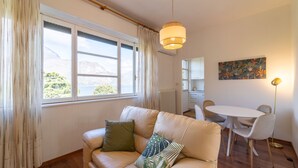 Un salon chaleureux avec un canapé beige, une table à manger avec des chaises, un luminaire suspendu et une vue sur les montagnes par la fenêtre.