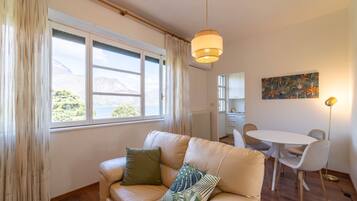 Una sala de estar acogedora con un sofá color beige, una mesa de comedor con sillas, una lámpara colgante y vistas a montañas a través del ventanal.