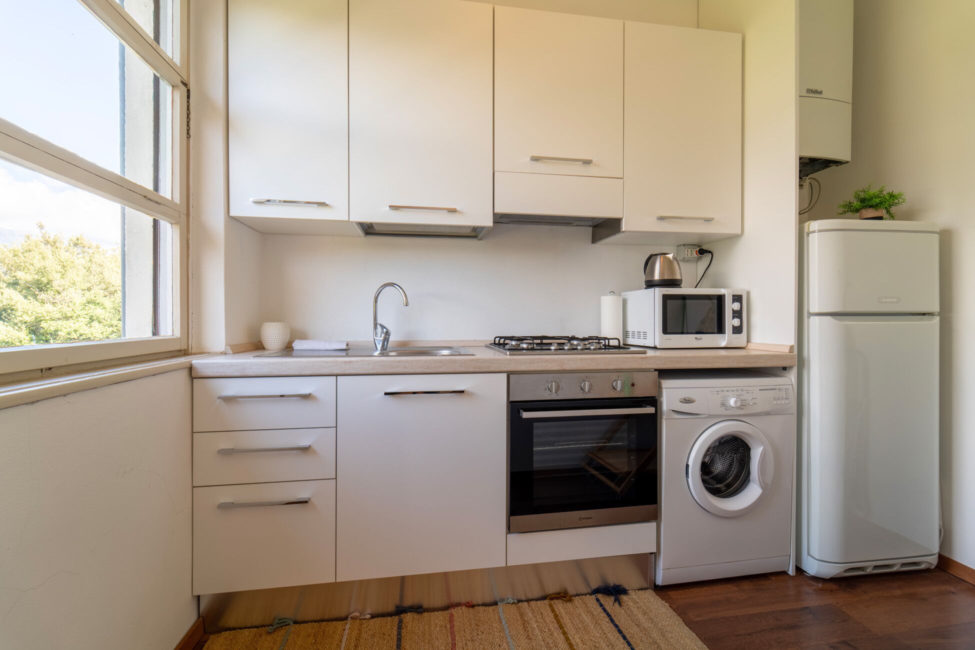 Een moderne keuken met witte kasten, een roestvrijstalen spoelbak, een gasfornuis, een magnetron, een wasmachine en een koelkast.