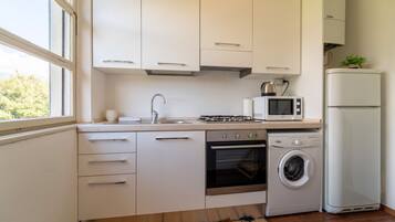 Een moderne keuken met witte kasten, een roestvrijstalen spoelbak, een gasfornuis, een magnetron, een wasmachine en een koelkast.