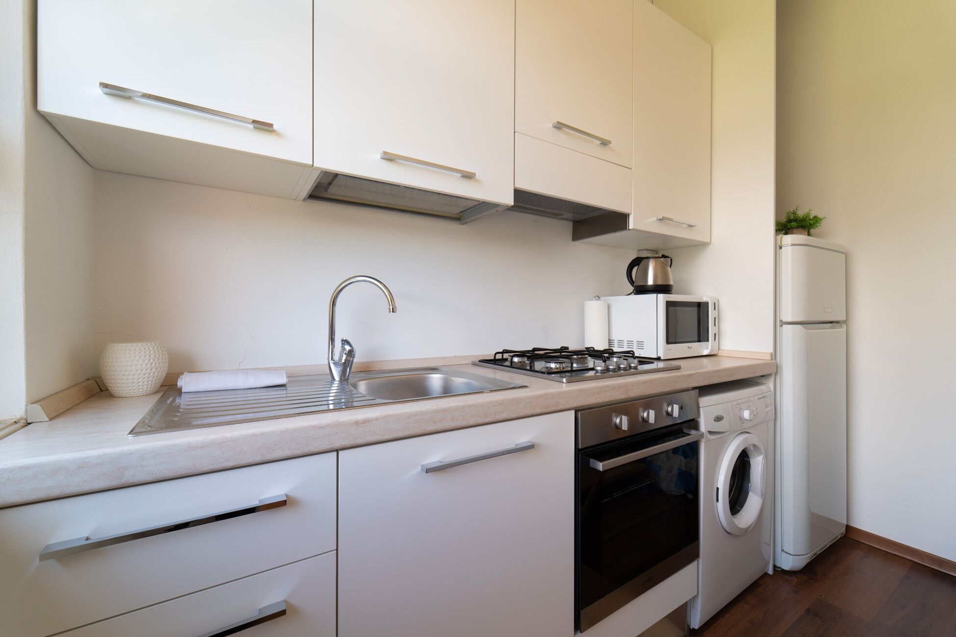 Eine moderne Küche mit weißen Schränken, Edelstahlgeräten, einer Spüle, einer Mikrowelle, einem Herd, einem Backofen und einer Waschmaschine.