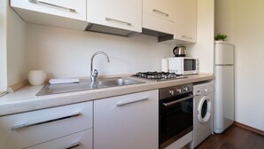 Une cuisine moderne avec des meubles blancs, des appareils électroménagers en acier inoxydable, un évier, un four à micro-ondes, une cuisinière, un four et un lave-linge.