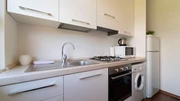 Eine moderne Küche mit weißen Schränken, Edelstahlgeräten, einer Spüle, einer Mikrowelle, einem Herd, einem Backofen und einer Waschmaschine.