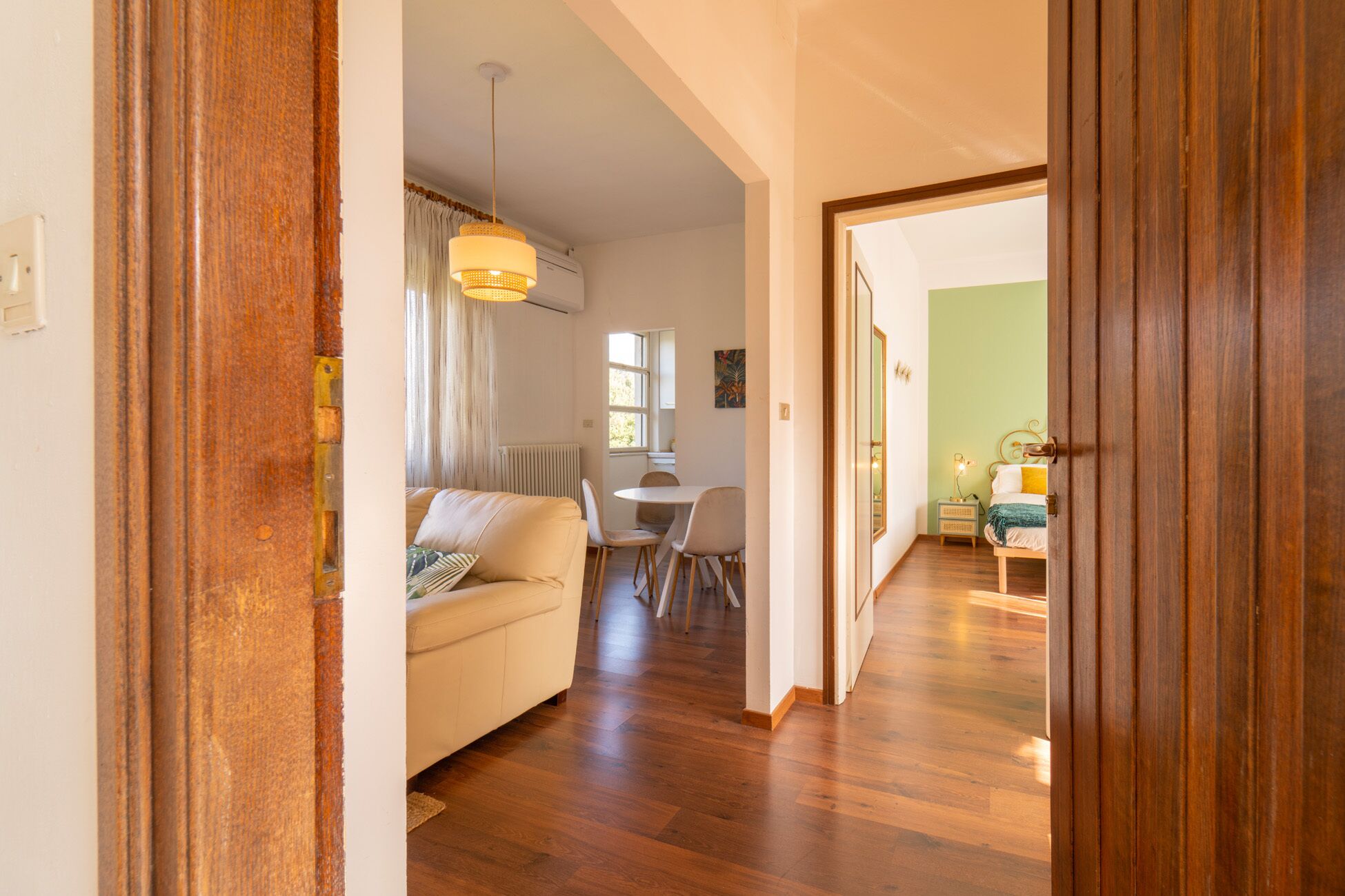 A living room with a sofa, a dining table with chairs, and a kitchen area visible through an open door.